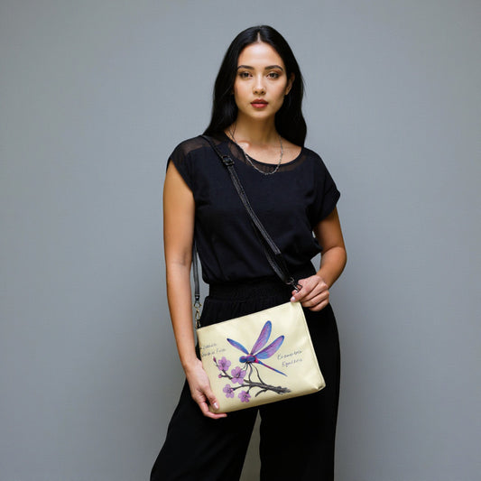 Modelo con bolso crossbody color crema estampado con libélula morada sobre rama, fondo gris claro”