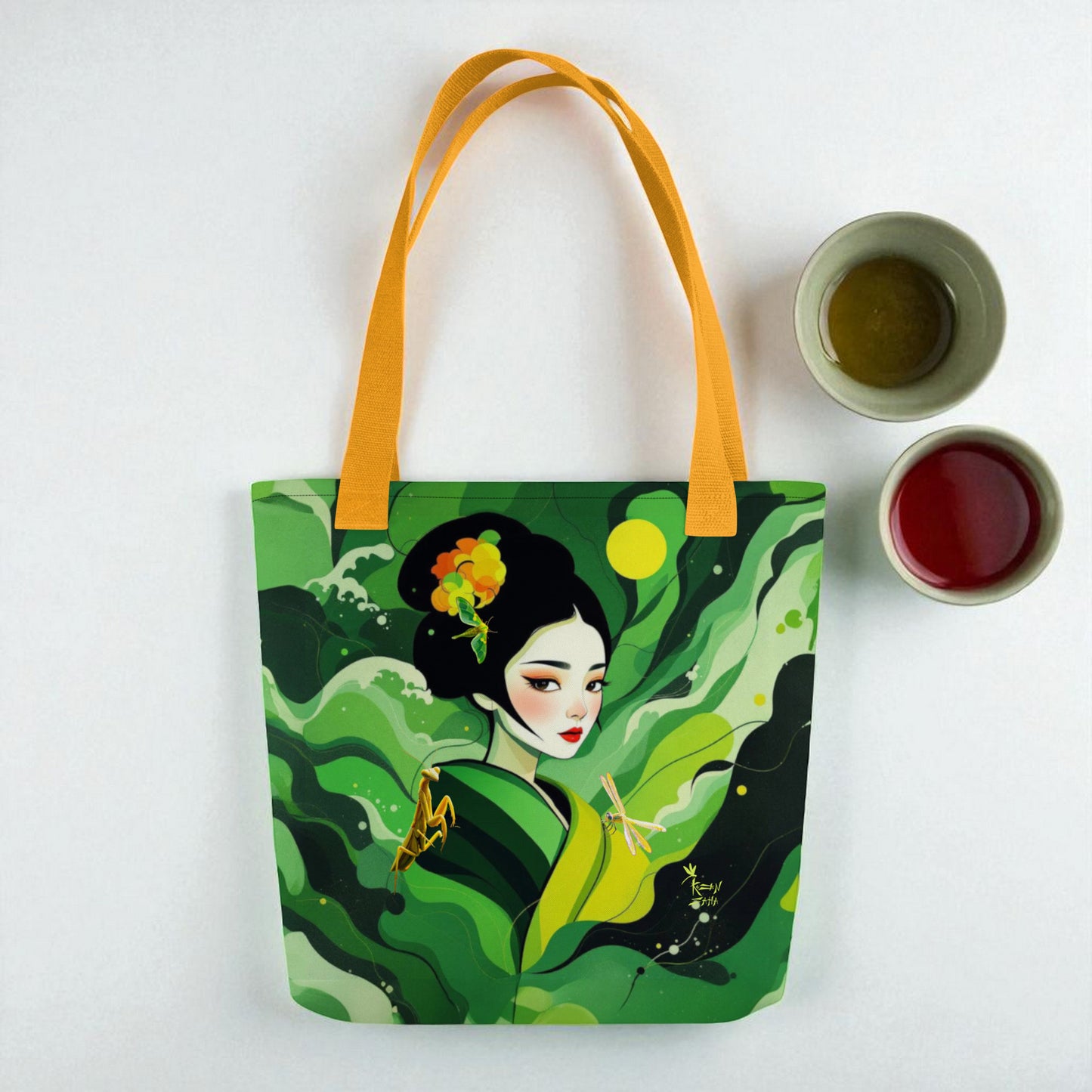 Bolso tote Geisha asas amarillas Esperanza sobre superficie blanca, composición lifestyle con hojas verdes y pequeñas tazas de té.