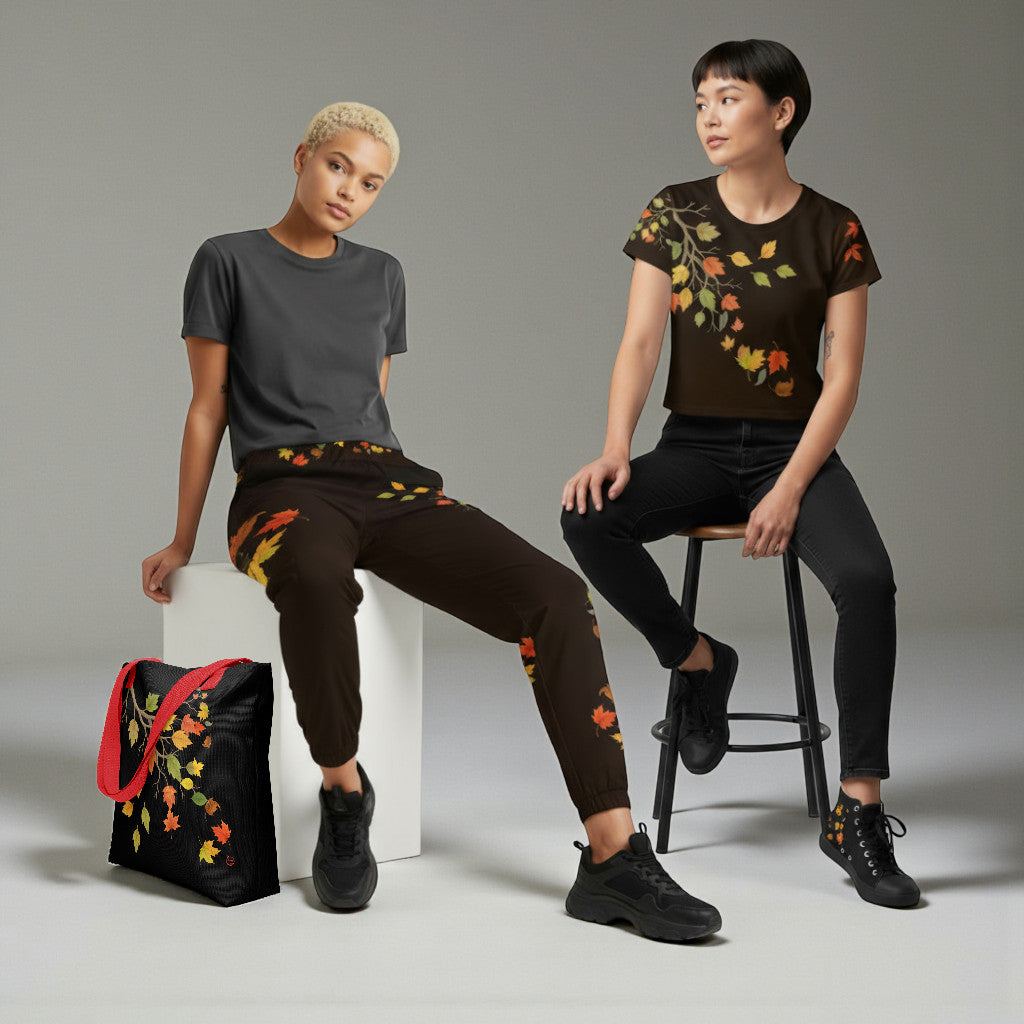 Dos modelos sentadas con conjunto de hojas otoñales (top y joggers) y bolso tote negro con borde rojo, fondo de estudio gris