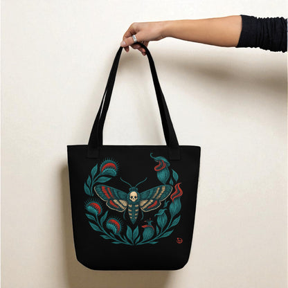 Mano sosteniendo bolso tote negro con polilla calavera, asas negras.