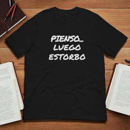 Camiseta negra unisex con frase Pienso luego estorbo en plano cenital sobre escritorio
