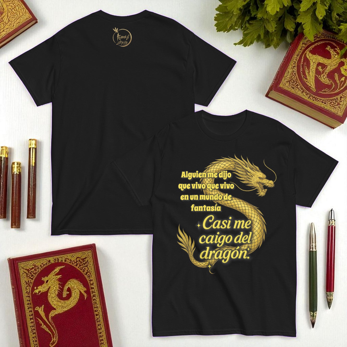 Camiseta negra unisex con dragon dorado y frase Casi me caigo del dragon en composicion flatlay