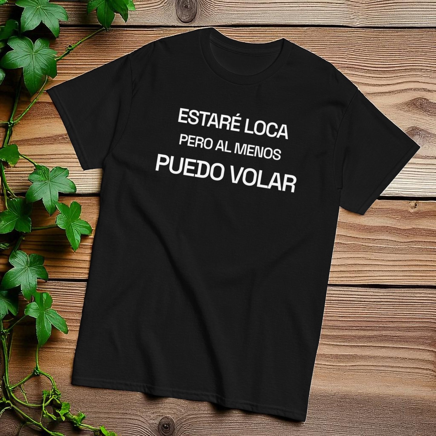 Camiseta negra tipografica con la frase estare loca pero al menos puedo volar sobre fondo de madera