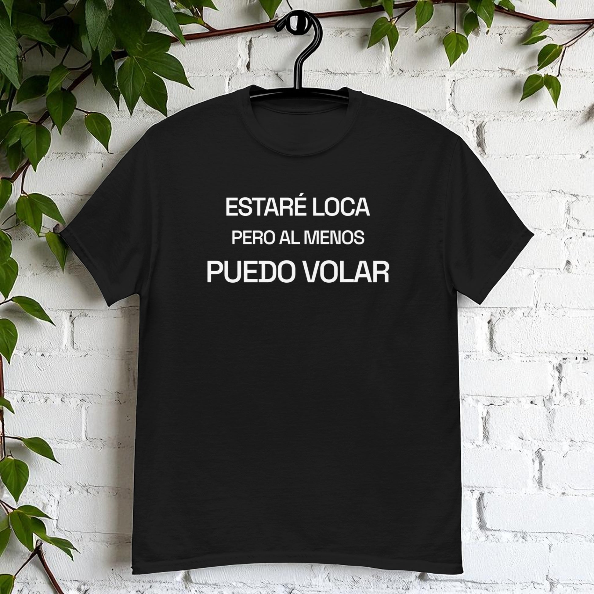 Camiseta negra en percha sobre pared blanca con la frase estare loca pero al menos puedo volar