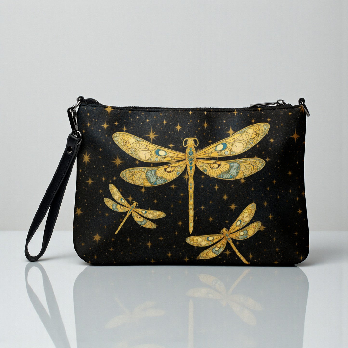 Bolso crossbody negro con libélulas doradas, vista frontal sobre superficie clara