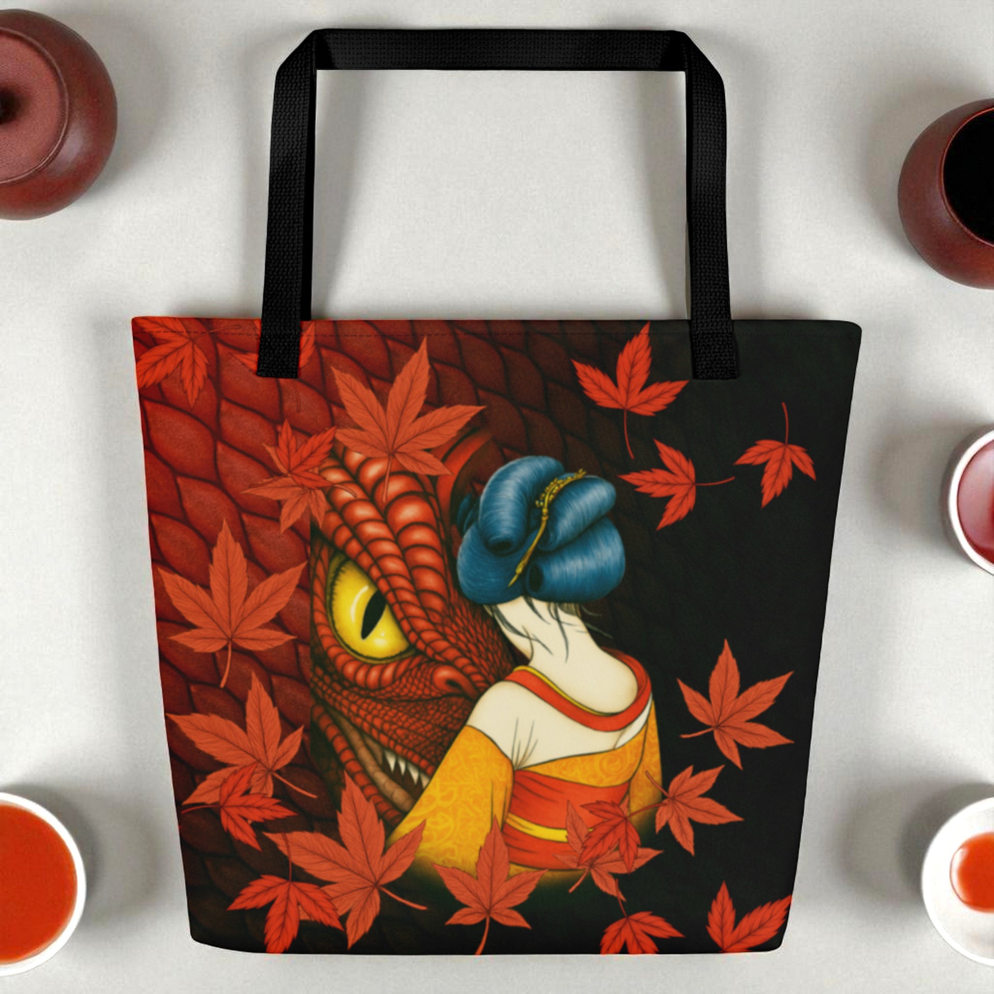 Bolso tote La mirada del Dragón sobre fondo blanco con pequeñas piezas de cerámica, composición minimal, asas negras.