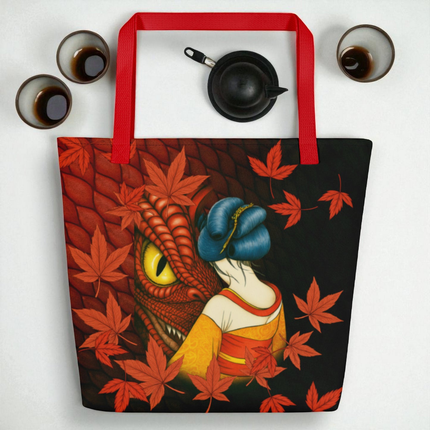 Bolso tote La mirada del Dragón sobre fondo blanco con pequeñas piezas de cerámica, composición minimal, asas rojas.