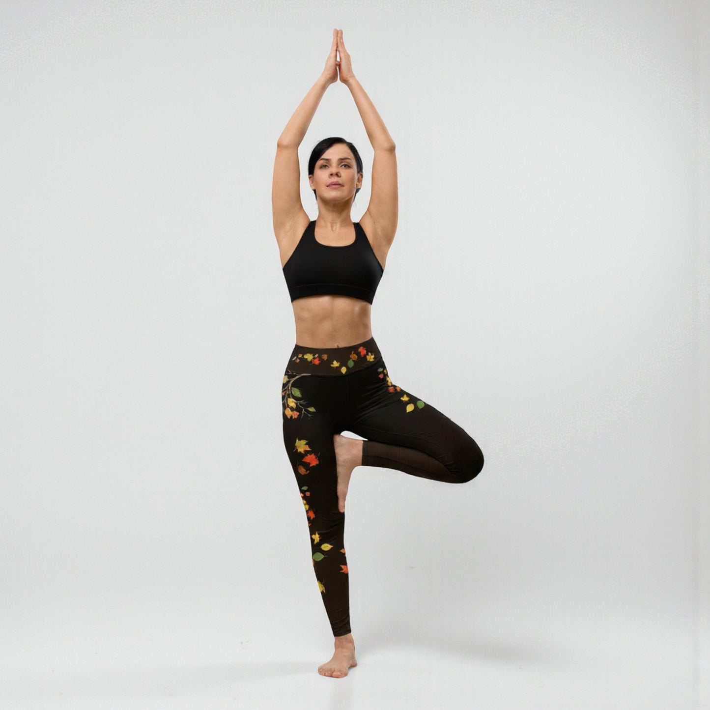 Postura de árbol yoga mostrando leggings negros con hojas otoñales