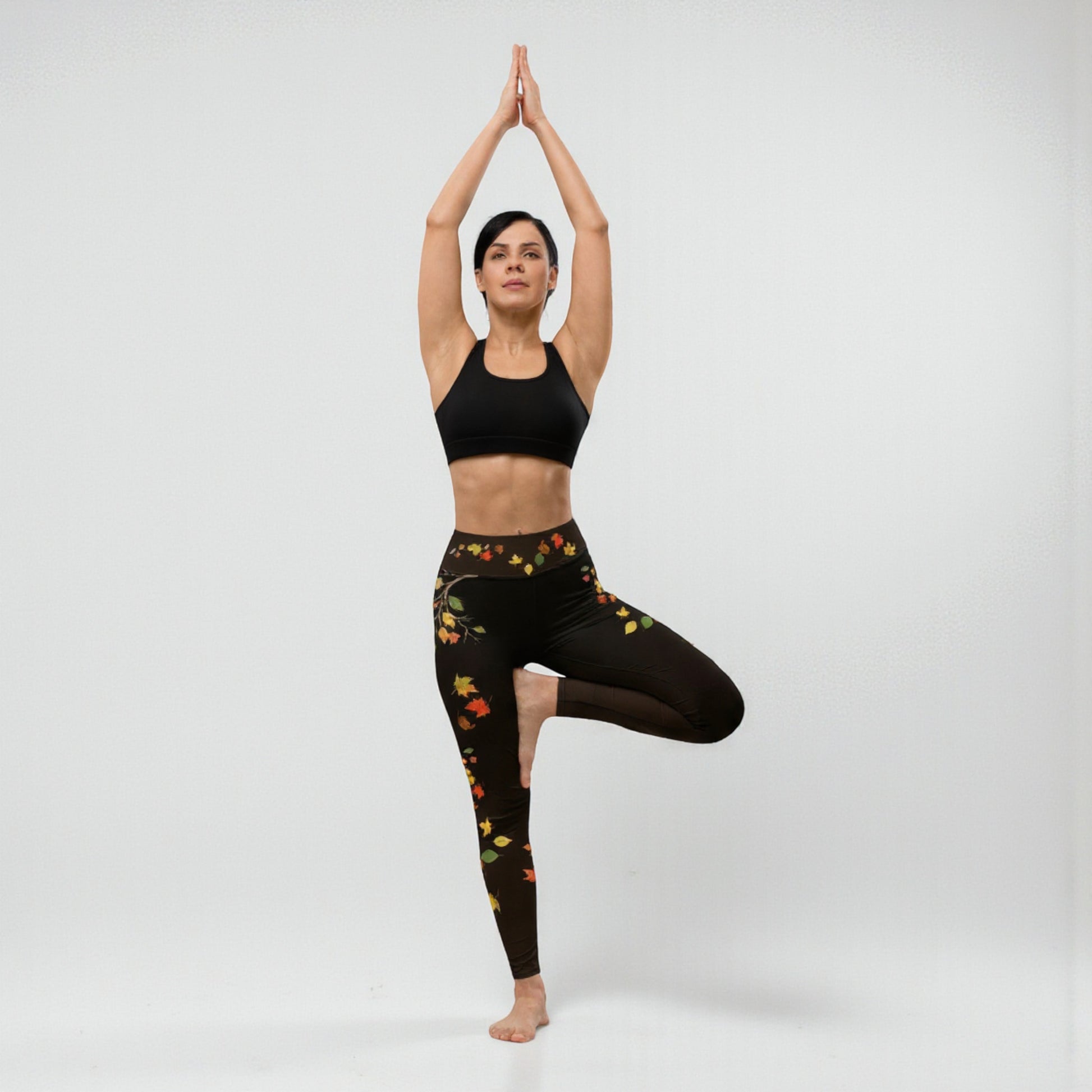 Postura de árbol yoga mostrando leggings negros con hojas otoñales