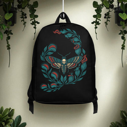Mochila negra con polilla calavera colgada frente a pared blanca con plantas verdes.