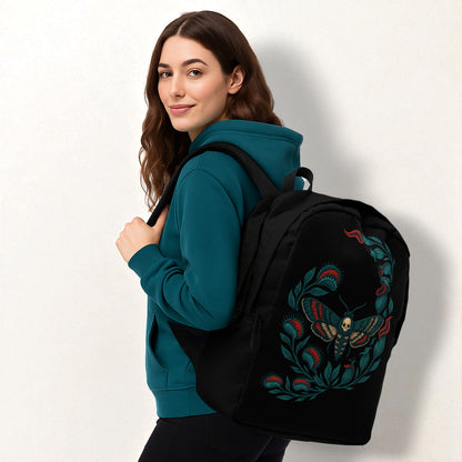 Mujer con sudadera azul petróleo y mochila negra con polilla calavera, vista de perfil sobre fondo claro.