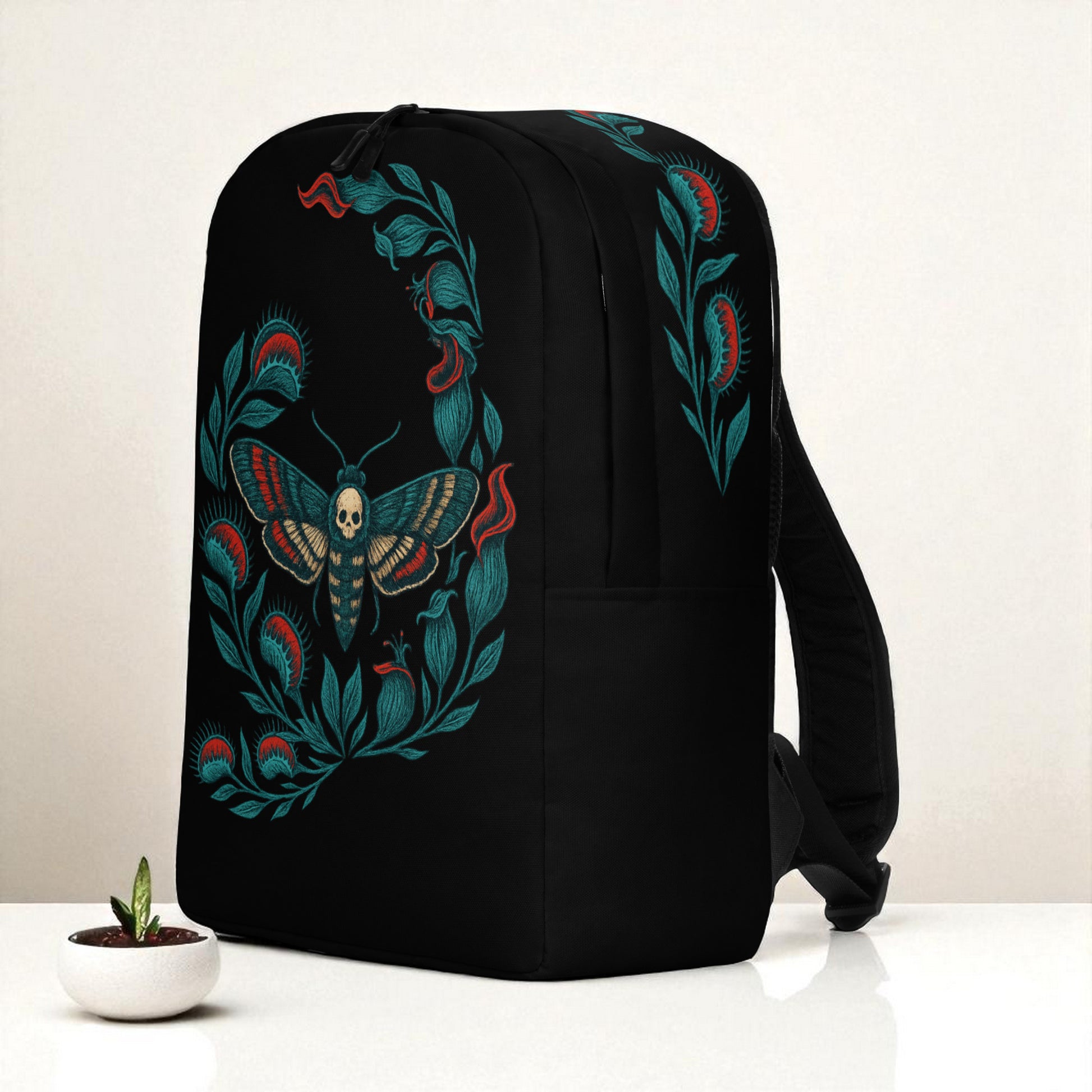 Mochila negra en vista tres cuartos derecha sobre mesa, con diseño en lateral de planta carnivora y diseño de polilla calavera.