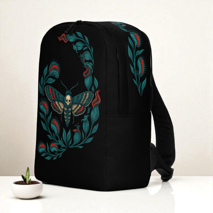 Mochila negra en vista tres cuartos derecha sobre mesa, con diseño en lateral de planta carnivora y diseño de polilla calavera.