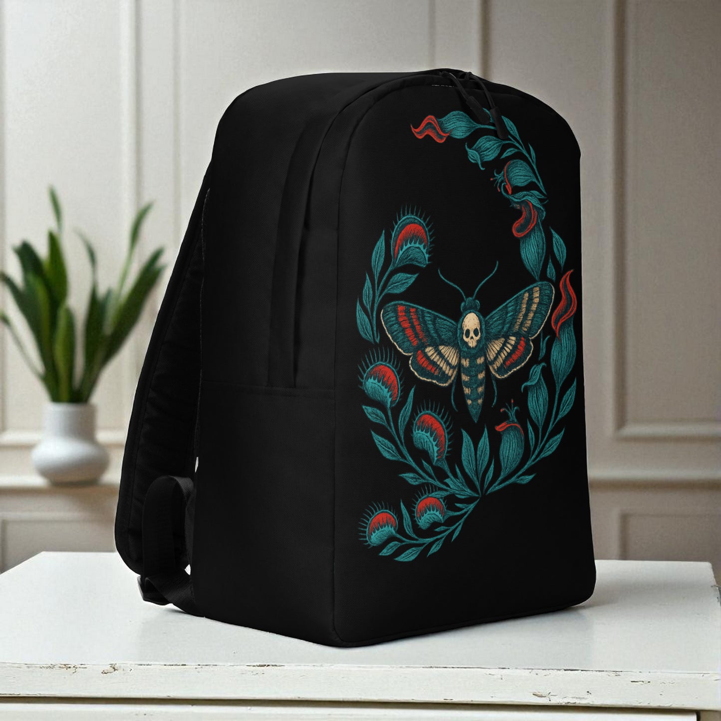 Mochila negra en vista tres cuartos derecha sobre mesa, con correa lateral y diseño de polilla calavera.