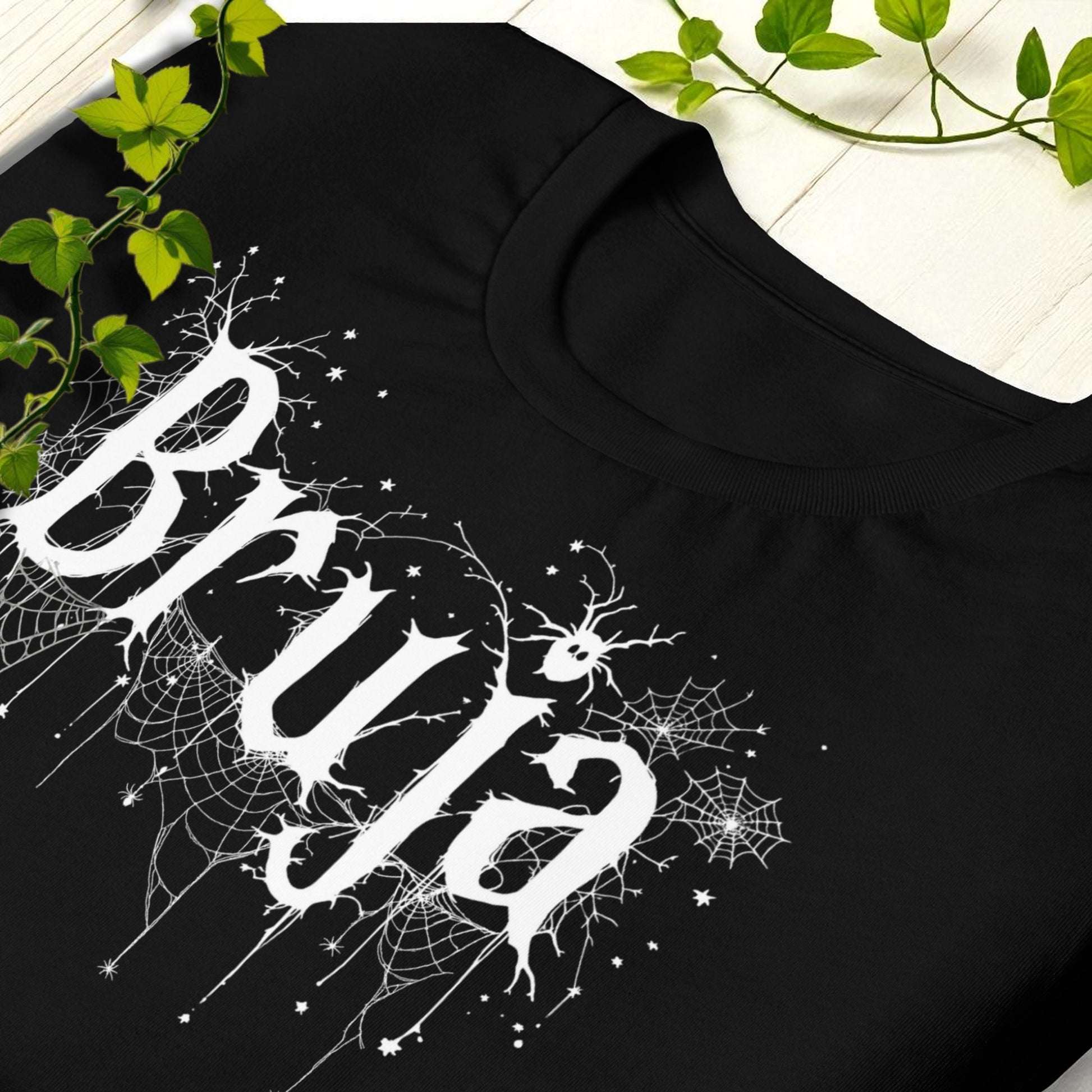 Detalle de cuello y hombro con diseño de telarañas en camiseta negra Bruja.