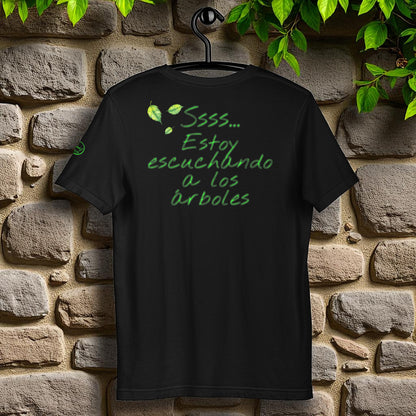 Camiseta negra unisex “Ssss… estoy escuchando a los árboles”, espalda  en percha, fondo de piedra
